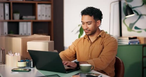 Man Working on Laptop at Desk with Packages