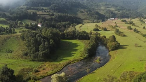 Slow fly over beautiful country river stream and green hills in backdrop