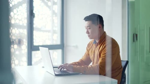 Side view Thoughtful asian businessman working typing on laptop while sitting at desk at workplace