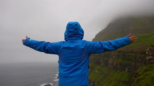 Man raising arms while enjoying view of foggy mountain in Gasadalur, Faroe Islands. Back view, stati