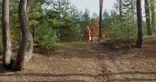 A Middleaged Woman Walks with a Dog in the Autumn Forest
