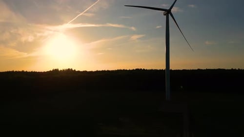 Large wind turbines with blades in field aerial view bright orange sunset blue sky wind park slow mo
