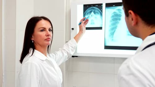 Doctora apunta con bolígrafo a las imágenes de rayos X mientras consulta con un colega masculino