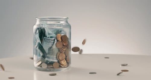 Money Falling Into Glass Jar of Savings