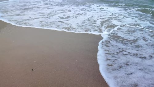 Sea Waves with White Foam Roll on the Sandy Beach of the Seashore Closeup