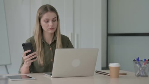 Woman Using Phone and Laptop at Desk