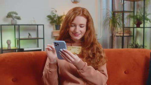 Happy Young Woman Using Credit Bank Card and Smartphone While Shopping Online Sitting on Sofa Couch