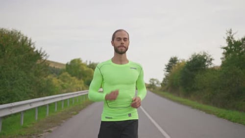 Smiling Runner Handsome Man in Green Bright Sportswear Running on the Country Road Outside Athletic