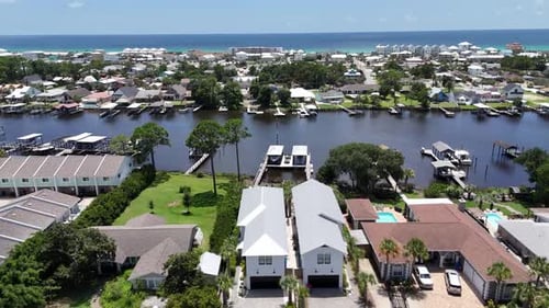 Crossing drone movement over the canal front homes with boat docks and waterfront lawns under blue s