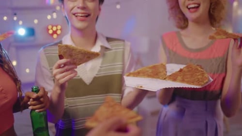Friends eating pizza at indoor celebration at night