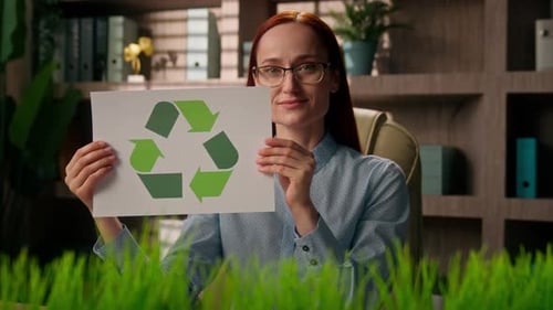 Mujer de negocios positiva que sostiene letreros de reciclaje para clasificar papel en la oficina