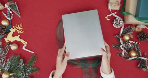 Top view of girl hands unpacking present gift box winter christmas decorations on red background.