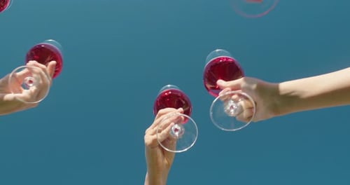 Des mains qui font tinter des verres de vin rouge sur un ciel bleu clair capturé depuis un angle bas