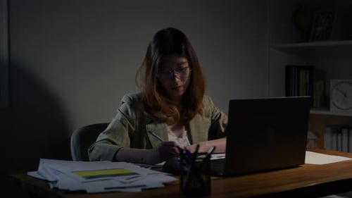 Asian businesswoman or freelancer working hard at the night looking the laptop digital tablet