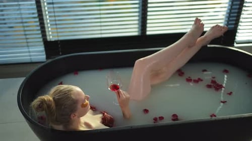 Spa Relaxation Woman Lying in Bath with Holding Glass with Red Wine Girl Relaxing in Bathroom at