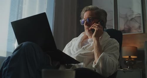 Man in Robe Talking on Phone with Laptop