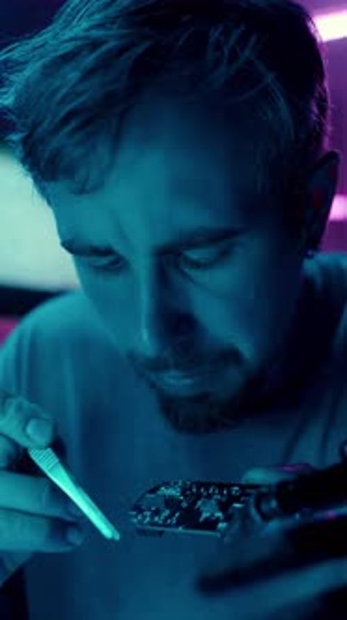 Man Soldering Circuit Board in Dark, Blue Room