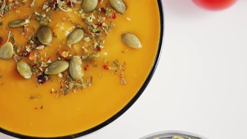 Autumn pumpkin cream soup close-up seasoned with aromatic spices and pumpkin seeds.