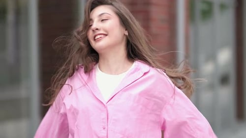 Cheerful woman twirling, smiling with pink shirt outside