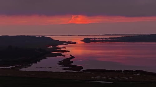 Movimiento suave hacia adelante a través de aguas tranquilas hacia una puesta de sol de color rojo y naranja vivos con árboles oscuros