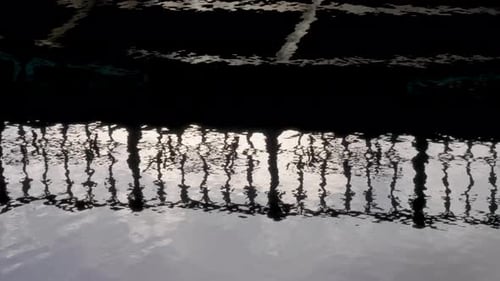 Close up water surface reflection promenade steel guards, silhouette on river