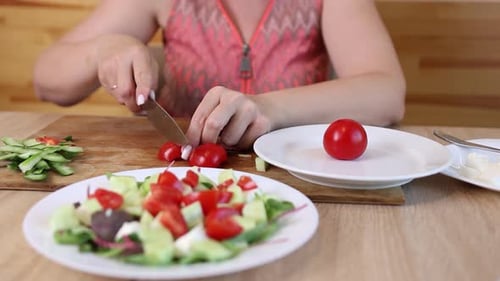 07 1Frau schneidet frische rote Tomaten auf einem Schneidebrett in Scheiben und legt sie auf einen Salatteller mit Gurken,