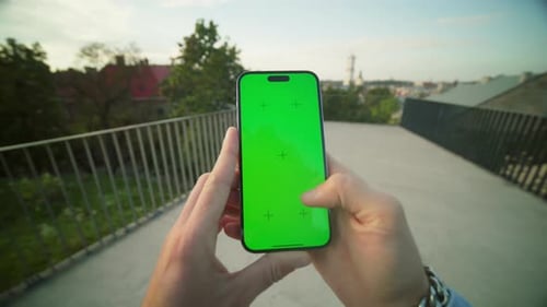 Closeup Shot of Man's Hand Holding Mobile Phone with Mockup and Green Screen While Scrolling Social
