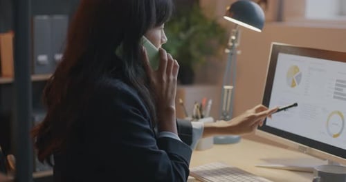Ambitious Businesswoman Speaking on Mobile Phone and Looking at Computer Screen Working in Office in