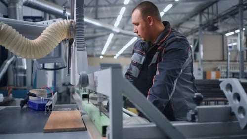Travailleur sciant des détails en bois par une machine de découpe automatisée dans un atelier d'usine de meubles