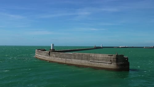 Vista serena del rompeolas costero en el puerto bajo un cielo azul claro durante un día soleado
