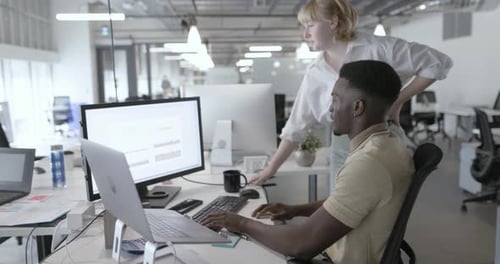 Businesswoman Approaching Businessman Working at Computer in Office Approach