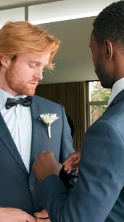 Vertical video: Best man bringing pin, pinning on groom adjusting bow tie for wedding in suite