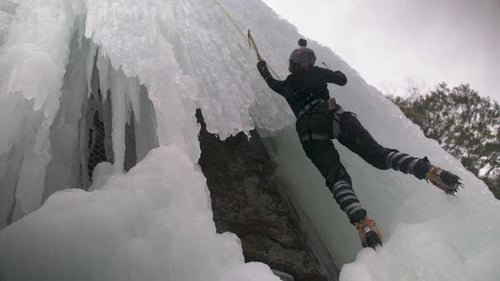 Low angle view of a person ice climbing a dangerous frozen waterfall