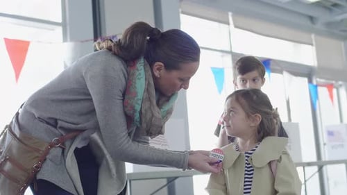 Mother Placing Voting Button on Daughter in American Polling Place Adult