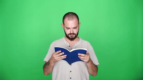 tattooed man reading blue book in front of green screen