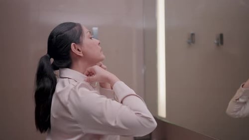 Woman Buttons Pink Shirt in Bathroom Mirror
