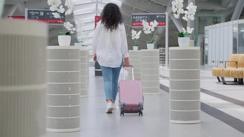 Female Traveler with Rolling Suitcase Walking in Station Hall