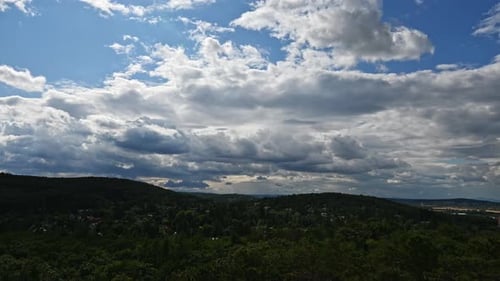 Time lapse of a dramatic sky filled with thick clouds stretches above a landscape of lush green hill