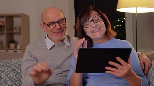 Senior couple video chatting on tablet in living room