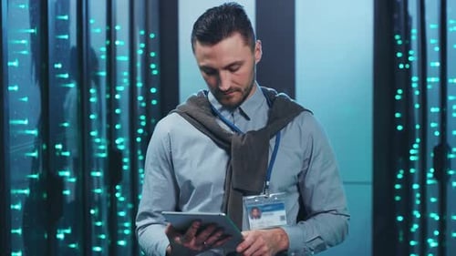 Un homme vérifie les données d'une tablette dans une salle de serveurs pour assurer le fonctionnement du réseau