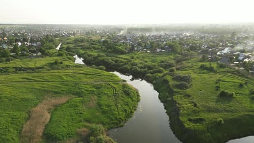 Winding River Flowing Through Misty Countryside Revealing Peaceful Small Town Nestled Among Lush