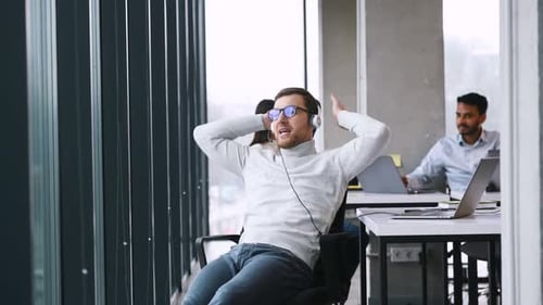 Un homme détendu est assis sur la chaise et parle à l'aide d'un casque. Les gens d'affaires travaillent ensemble