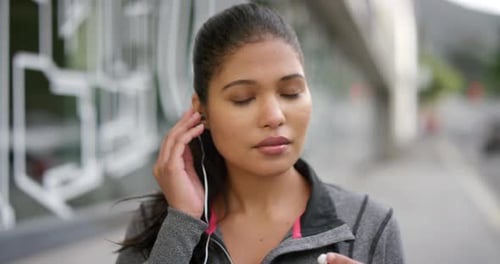 Portrait of an active woman listening to music in earphones outside in a modern city