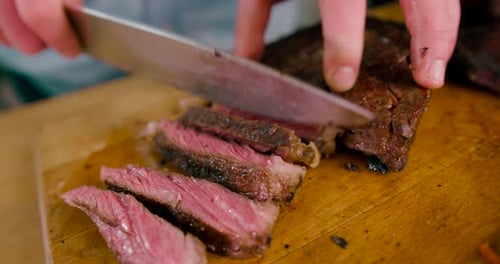 Close up view of Male hand with a knife slicing the Grilled Beef Steak on cutting Board on Wooden Ba