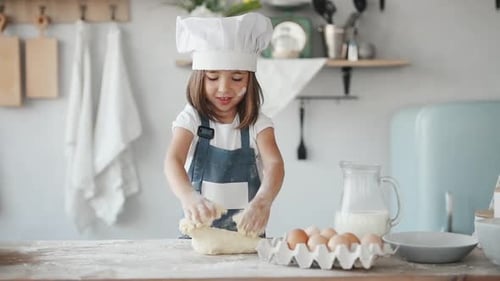 Cute kid in white chef uniform kneading the dough on the kitchen