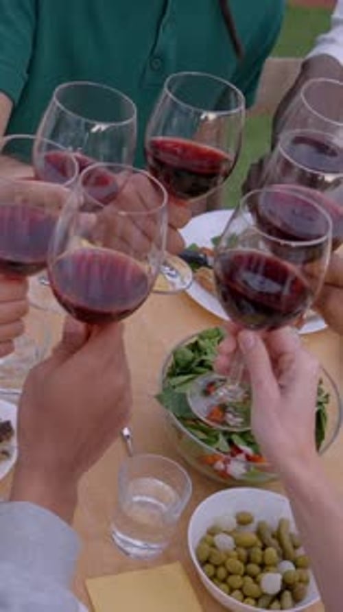 Close Up of Hands Toasting with Red Wine on Table Full of Food Gathering of Unrecognizable Friends