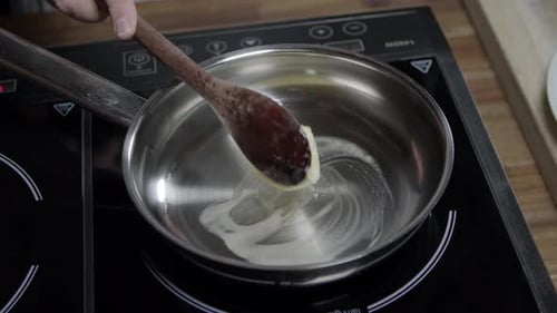Chef adds butter with a spoon in hot pan to prepare cafe de paris butter sauce, on induction stove