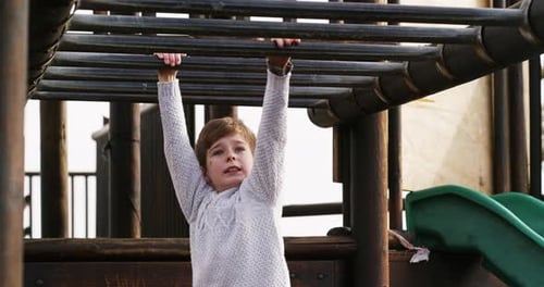 Boy climbing monkey bars on a jungle gym outdoors in a kids activity park during summer