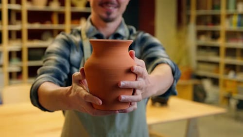 Man Presents Handmade Ceramic Pot in Bright Workshop