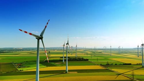 Enormous agricultural fields with wind farms. Multiple wind turbines producing clean energy.